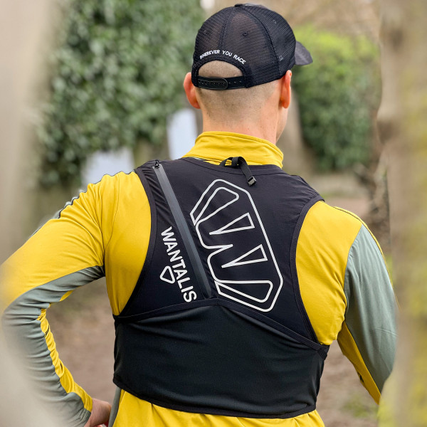 Läufer mit Trinkweste Läufer mit Hydrabag Elite 8L Trinkweste von hinten, schwarze Kappe mit Aufdruck, gelbes Langarmshirt, Blick in die Natur.