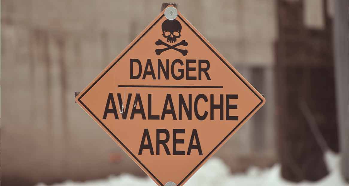 Ein oranges, rautenförmiges Warnschild mit schwarzer Schrift "DANGER AVALANCHE AREA" und Totenkopf-Symbol.