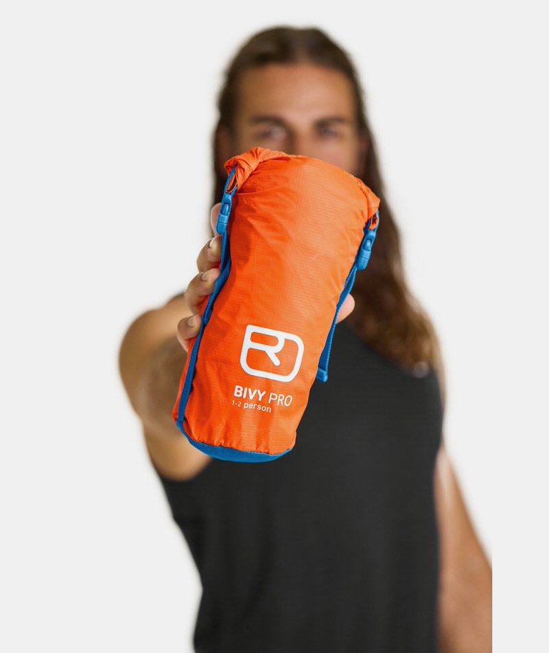 Sac de bivouac orange Ortovox Bivy Pro, emballé de manière compacte, tenu dans une main.