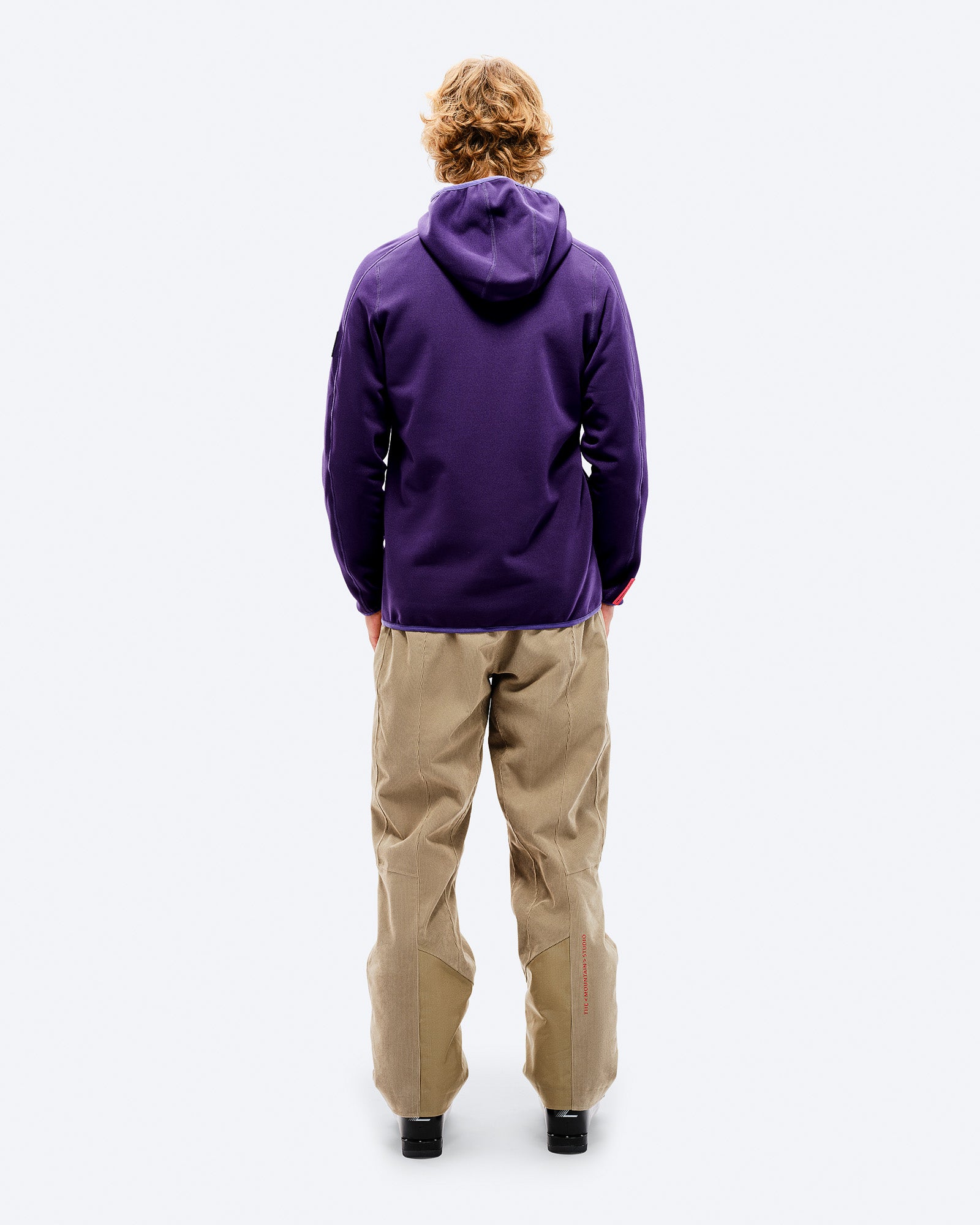 Lila Fleece-Hoodie Rückansicht Rückansicht einer Person mit lila Tech Fleece Hood und beigen Cordhosen vor weißem Hintergrund.