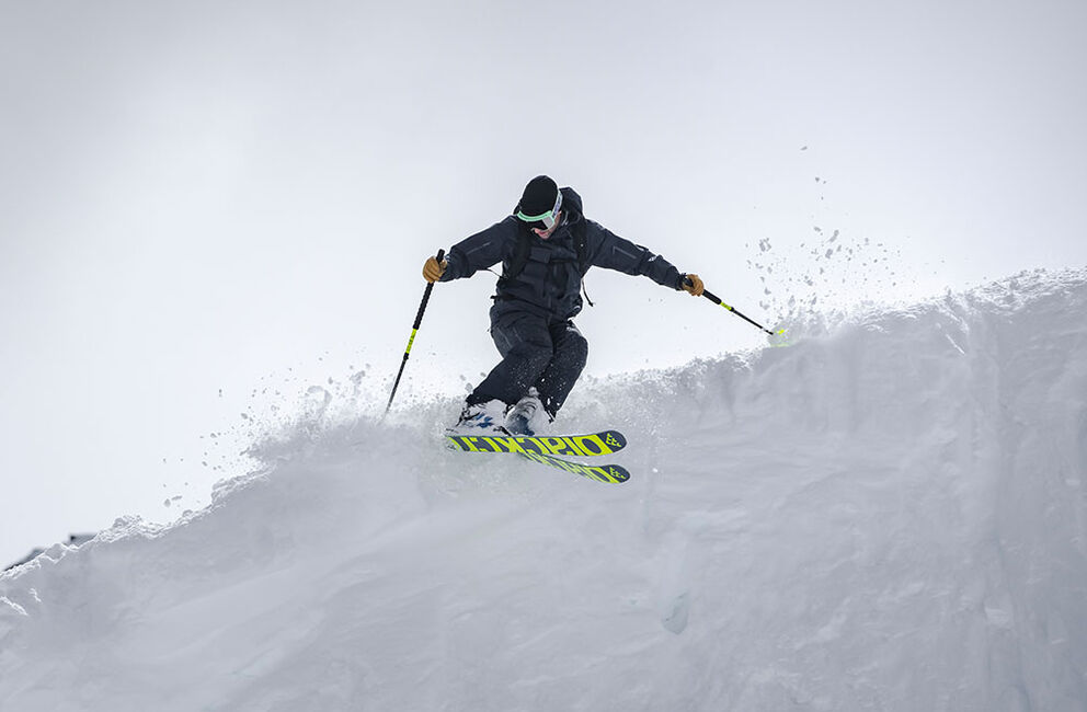 Skifahrer im Pulverschnee Skifahrer im Pulverschnee mit Black Crows Atris Ski in Aktion, Stöcke eingesetzt.