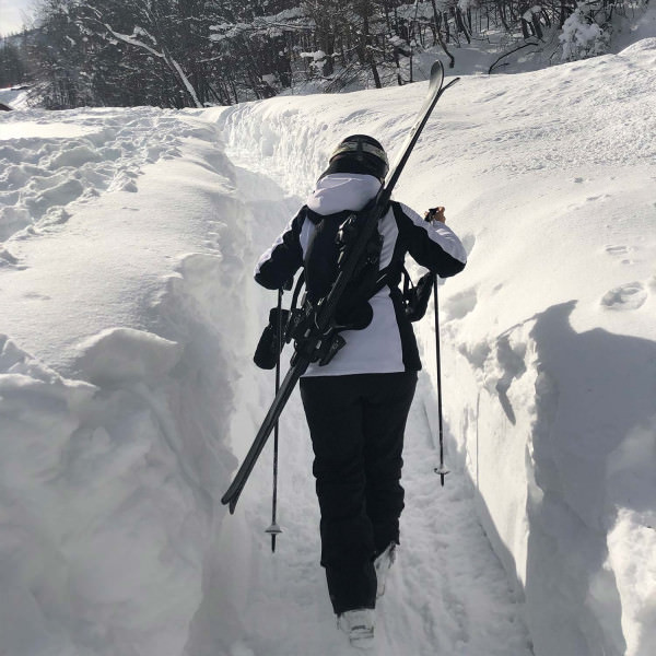 Skifahrer im Schnee Person mit Skiern auf dem Rücken und Skistock in der Hand geht durch den Schnee. Skiback ist sichtbar.
