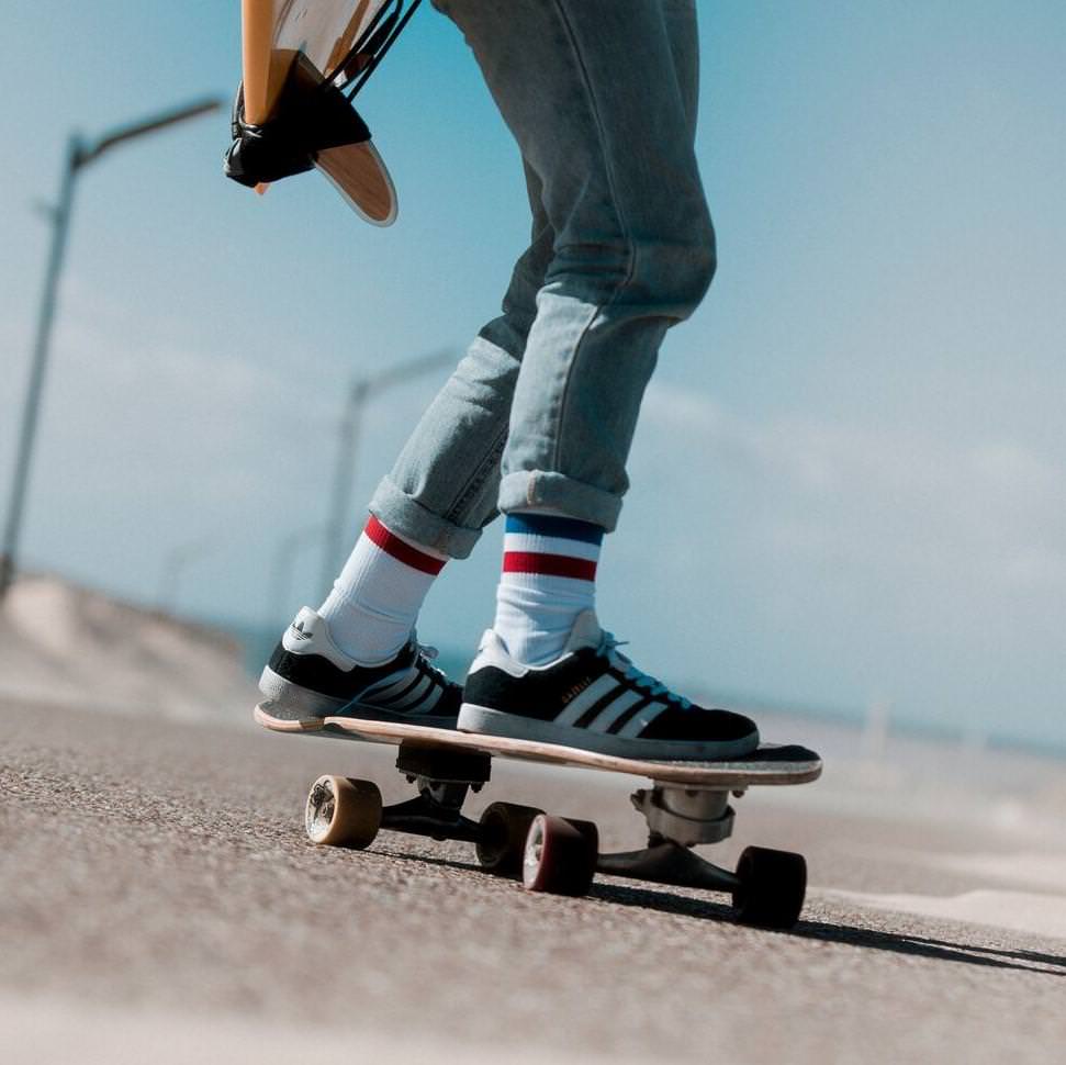 Skateboarder mit Sockeneinsatz Person auf Skateboard mit American Pride Mid High Socken, Jeans und Turnschuhen vor blauem Himmel.
