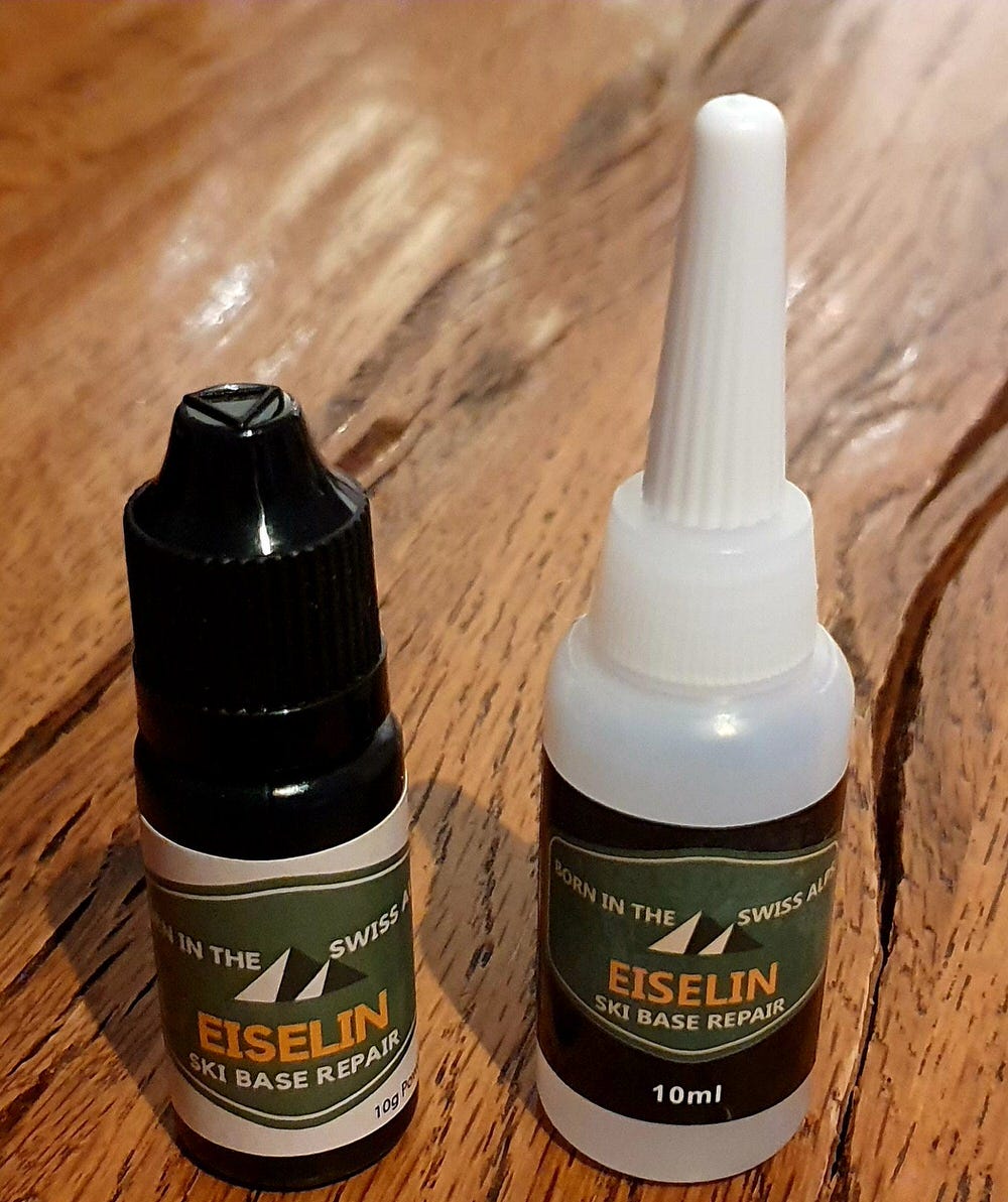 Zwei Flaschen: Schwarze Flasche Pulver, weiße Flasche Kleber für die Ski Belag Reparatur.