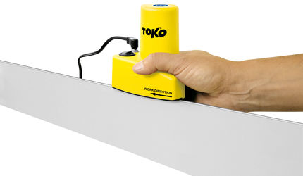 Skikanten Tuner Gerät Hand führt gelben Toko Edge Tuner über Skikante. Das Schleifgerät hat ein Stromkabel. Pfeil "Work Direction" auf dem Gerät.