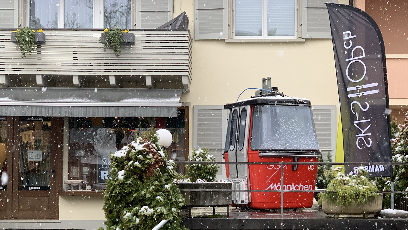 Rotes Gondel-Modell im Schnee Ein rotes Gondel-Modell vor einem Laden mit einem "Ski-Ob" Banner im Schneefall.