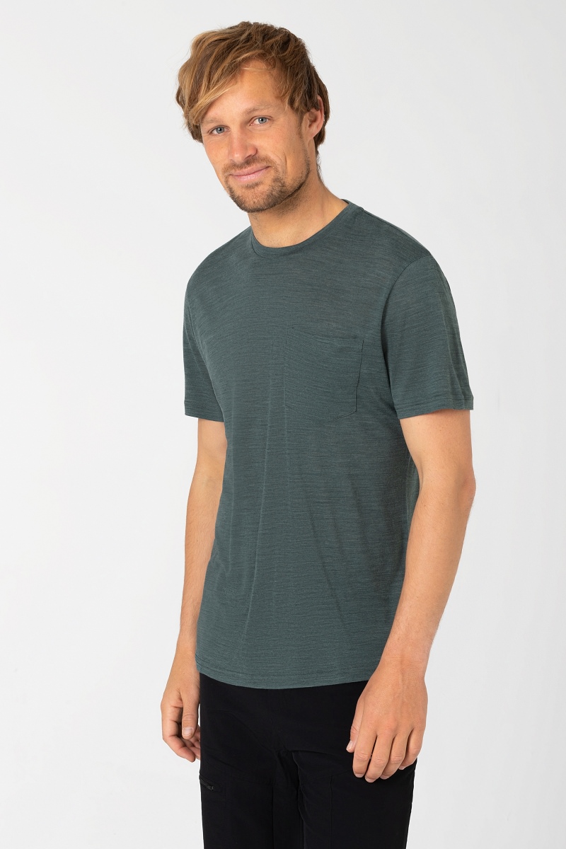 Mann trägt meliertes, petrolfarbenes T-Shirt mit Brusttasche und schwarze Hose. Lässig, Blick zur Seite.