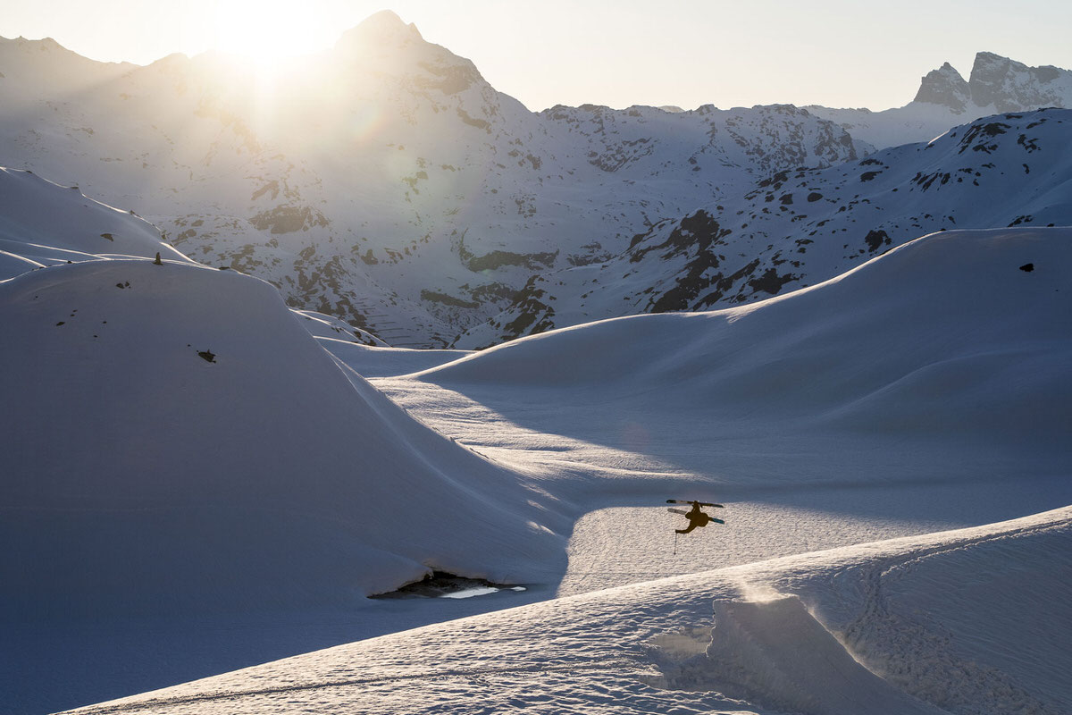 Verschneite Berglandschaft mit Skifahrer, der einen Sprung macht. Griffon 13 ID Bindung geeignet für Freestyle-Moves.