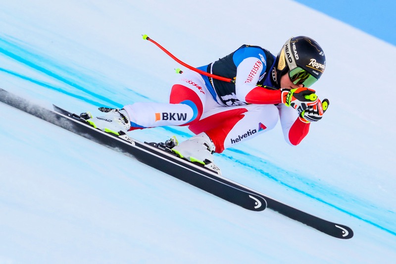 Skifahrer mit Helm und Brille in Abfahrtsposition auf der Piste.