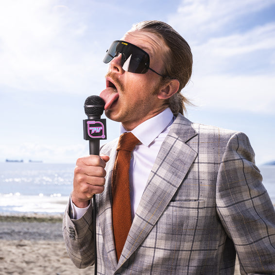 Homme avec lunettes de soleil, costume et cravate léchant un microphone sur la plage. Style "exec".