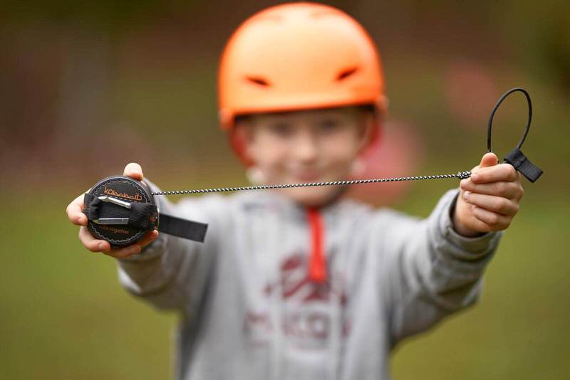 Kind mit Zugsystem Ein Kind mit orangenem Helm hält ein schwarzes Zugsystem in seinen Händen und präsentiert es in die Kamera.