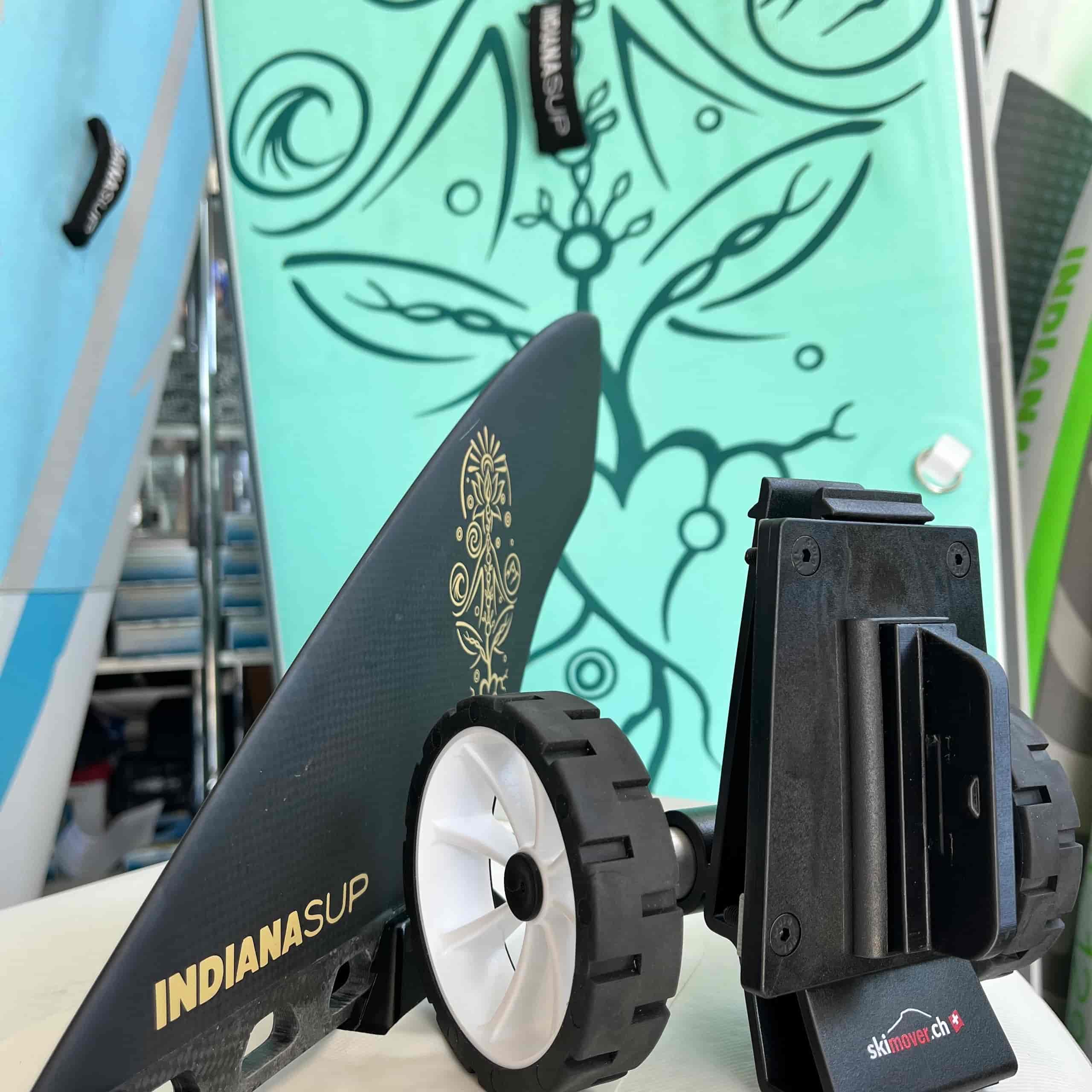SUPmover Räder und Halter SUPmover Räder, mit schwarzem Halter, weisser Felge, neben einer Finne und einem SUP Board.