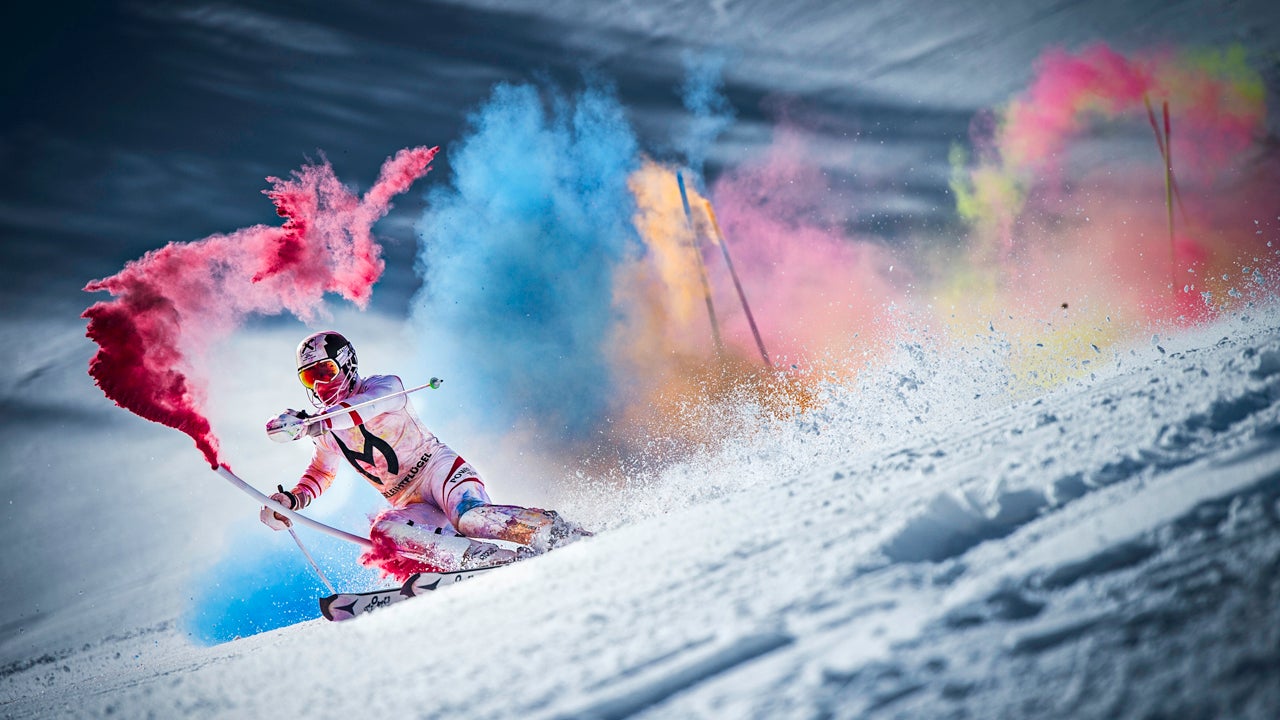 Marcel Hirscher Colours: Das Video Ein Skifahrer fährt einen verschneiten Hang hinunter, umgeben von farbigem Rauch in rot, blau, gelb und rosa.