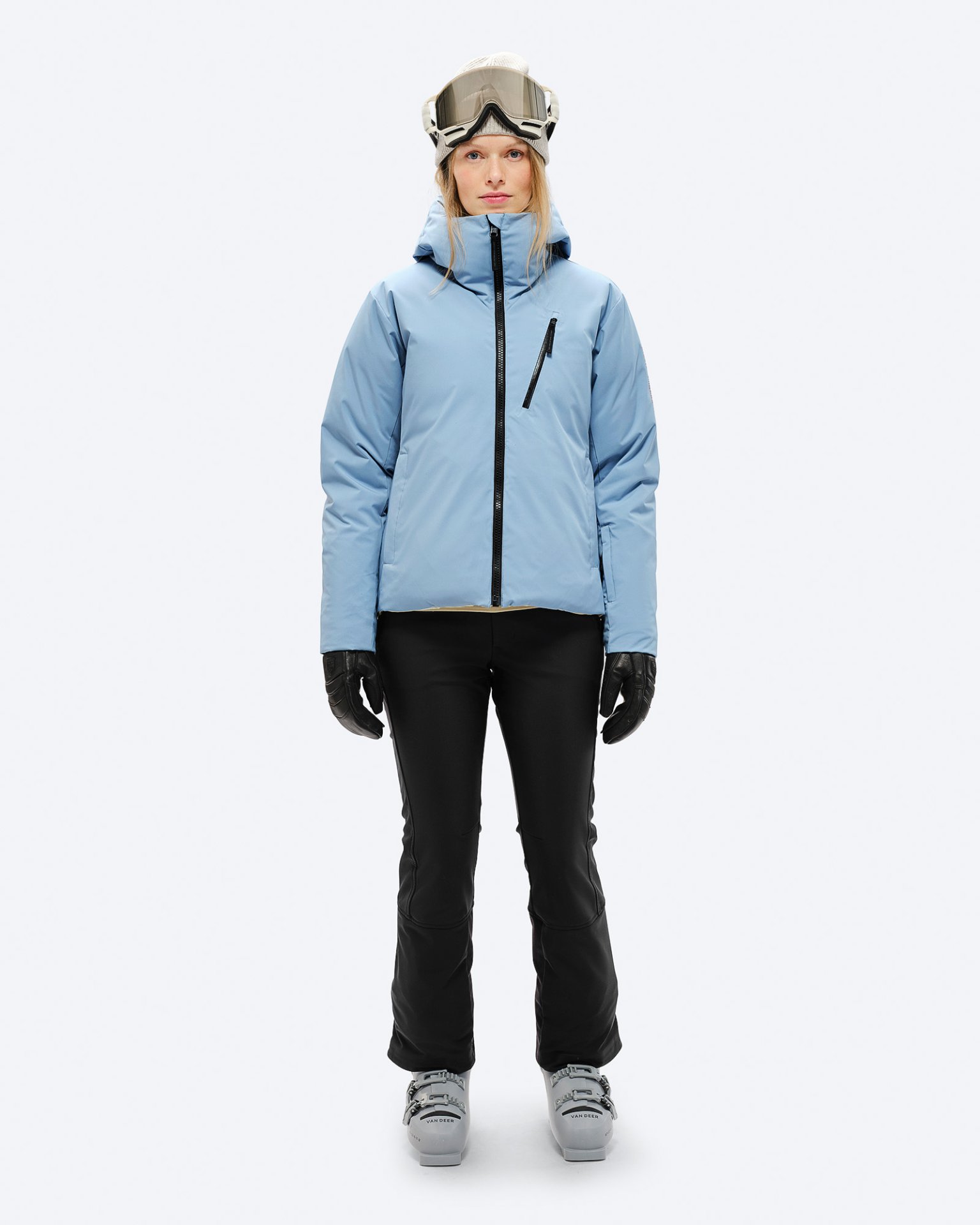 Skifahrer Outfit Person mit Skibrille, Daunenjacke in "Castle Wall", schwarzer Hose und Handschuhen, sowie Skischuhen.