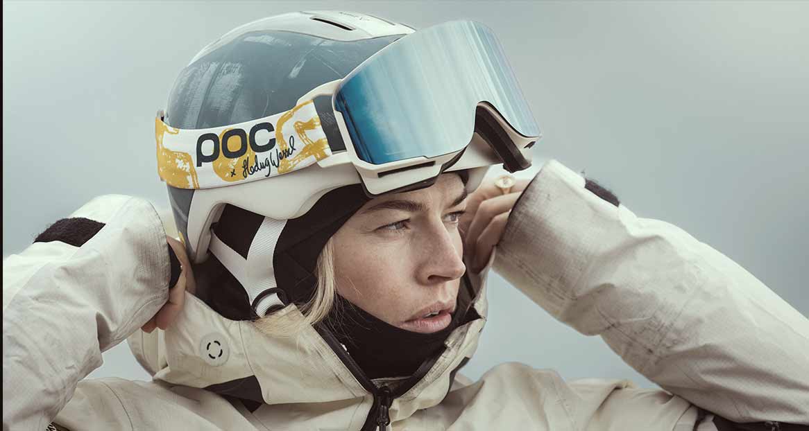 Frau mit Skihelm und -brille, die ihre Jacke zuzieht, Blick zur Seite.