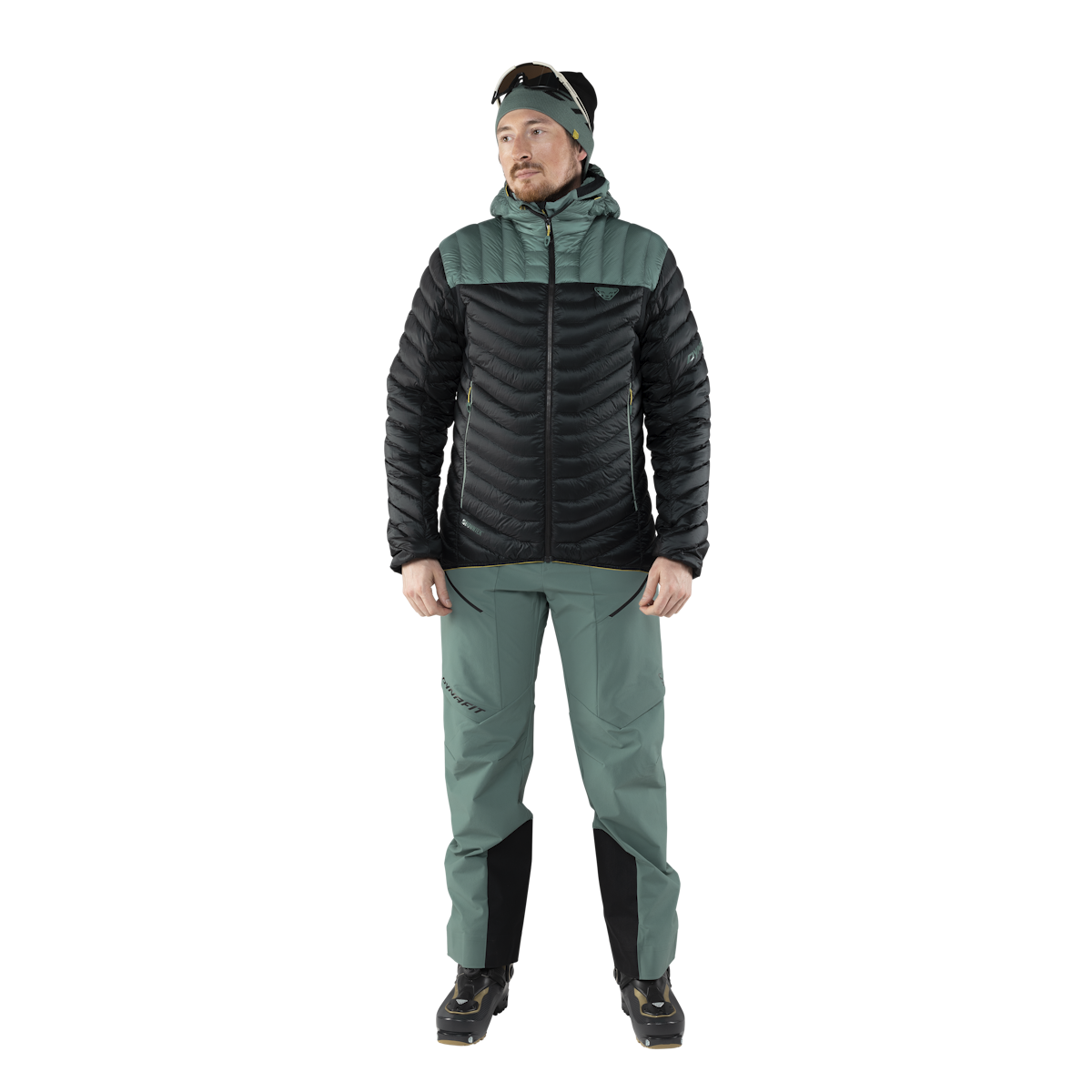 Mann in Daunenjacke und Skitourenhose, vor weißem Hintergrund. Die Jacke ist schwarz und grün.