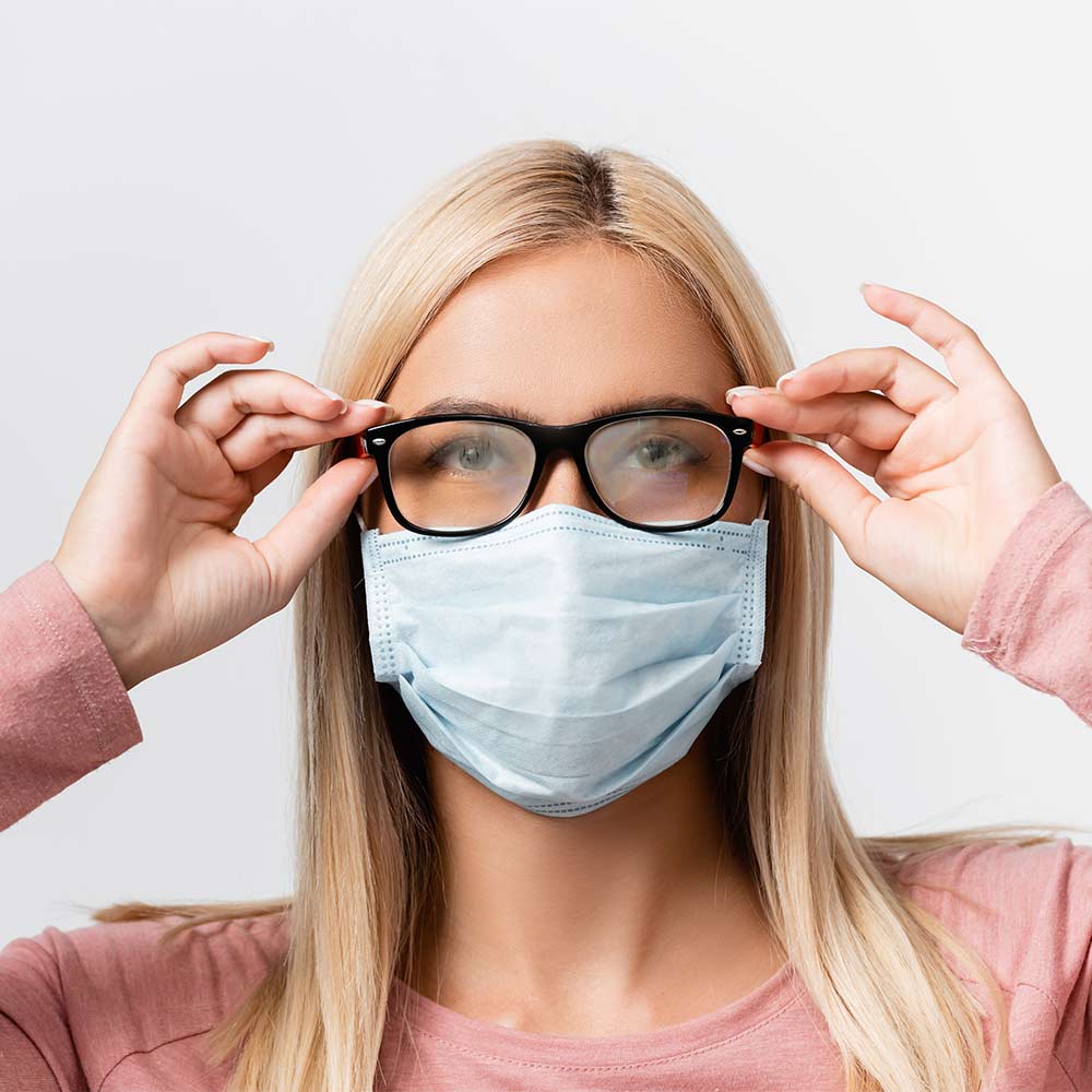 Frau mit Maske, deren Brille beschlagen ist. Fokus auf beschlagene Brillengläser. Fog-Out Antibeschlag Microfaser.