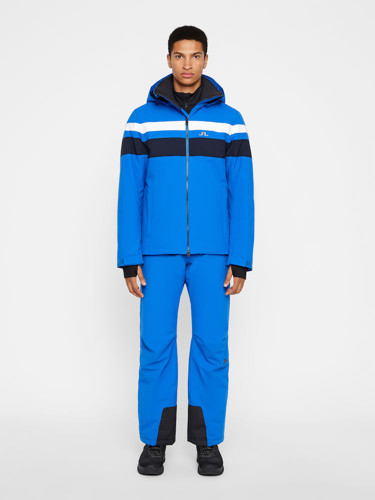 Skijacke Franklin blau Ein Mann trägt eine blaue J.Lindeberg Franklin Skijacke und Hose mit weißen und marineblauen Streifen.