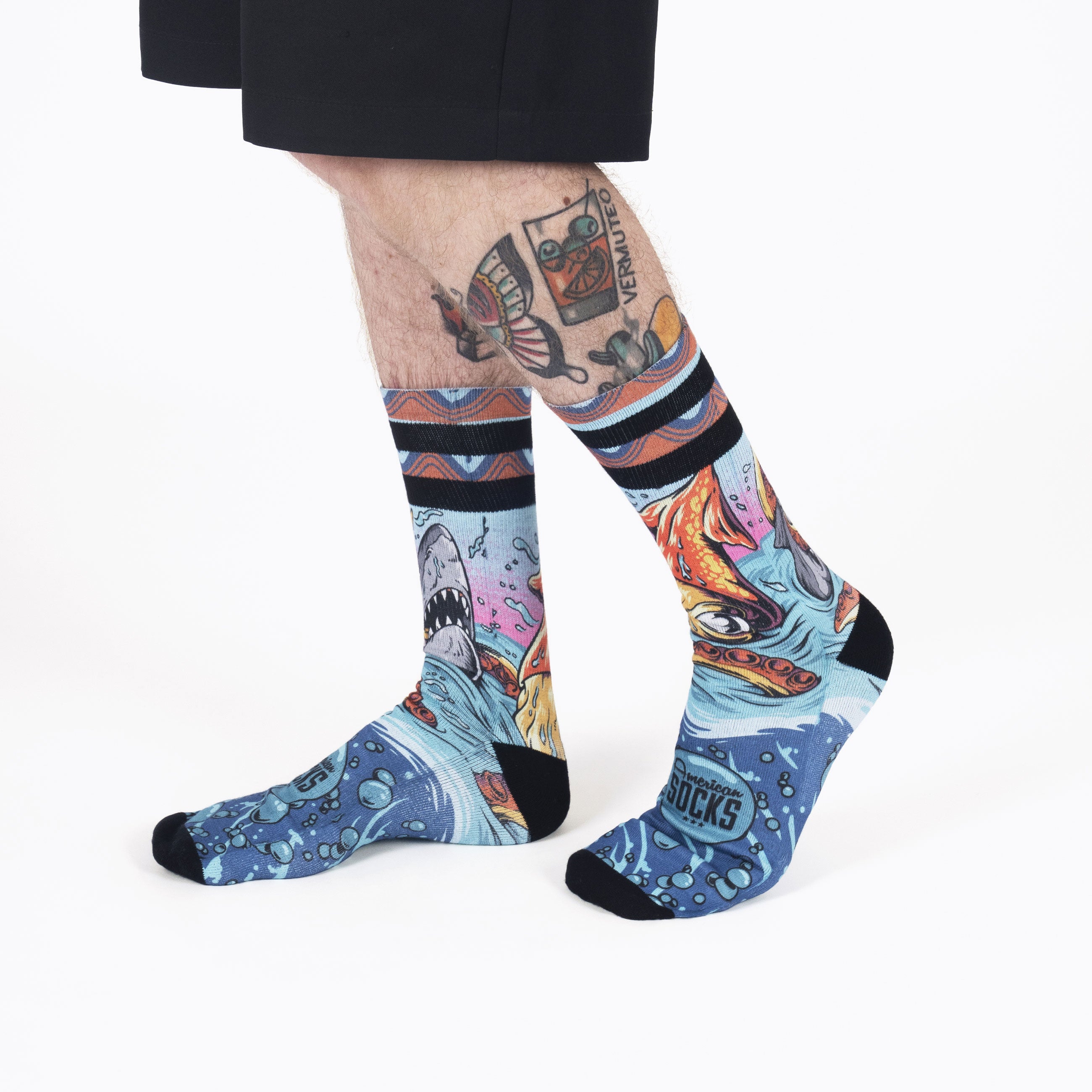 Chaussettes bleues Seamonsters Deux jambes aux mollets tatoués portent des chaussettes bleues `Seamonsters` avec des motifs de requin, de pieuvre et de bulles.