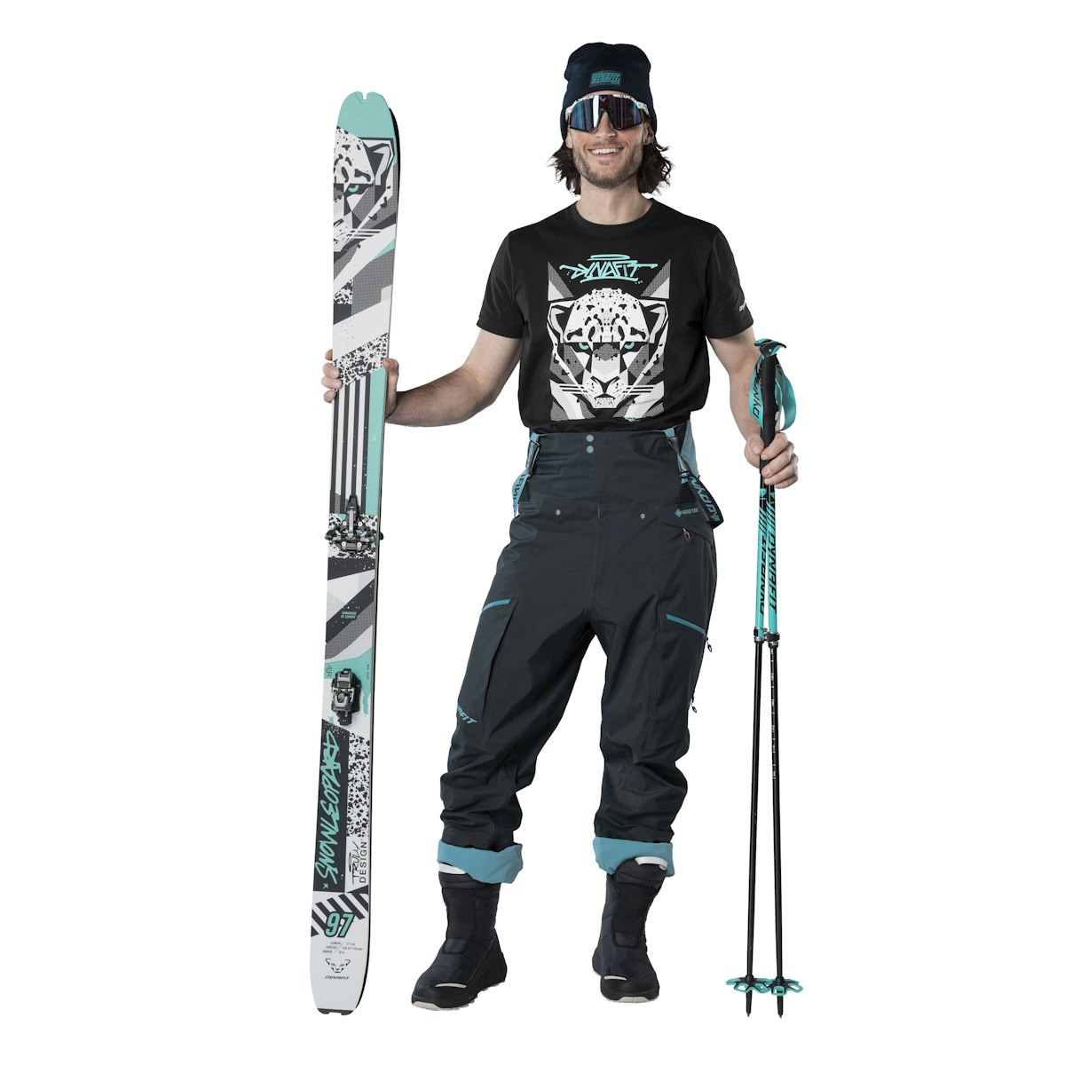 Dynafit Winter Bootie Skibekleidung: Mann mit Ski, Skistöcken, Mütze, Brille und T-Shirt mit Leopardenmotiv. Dunkle Skihose.