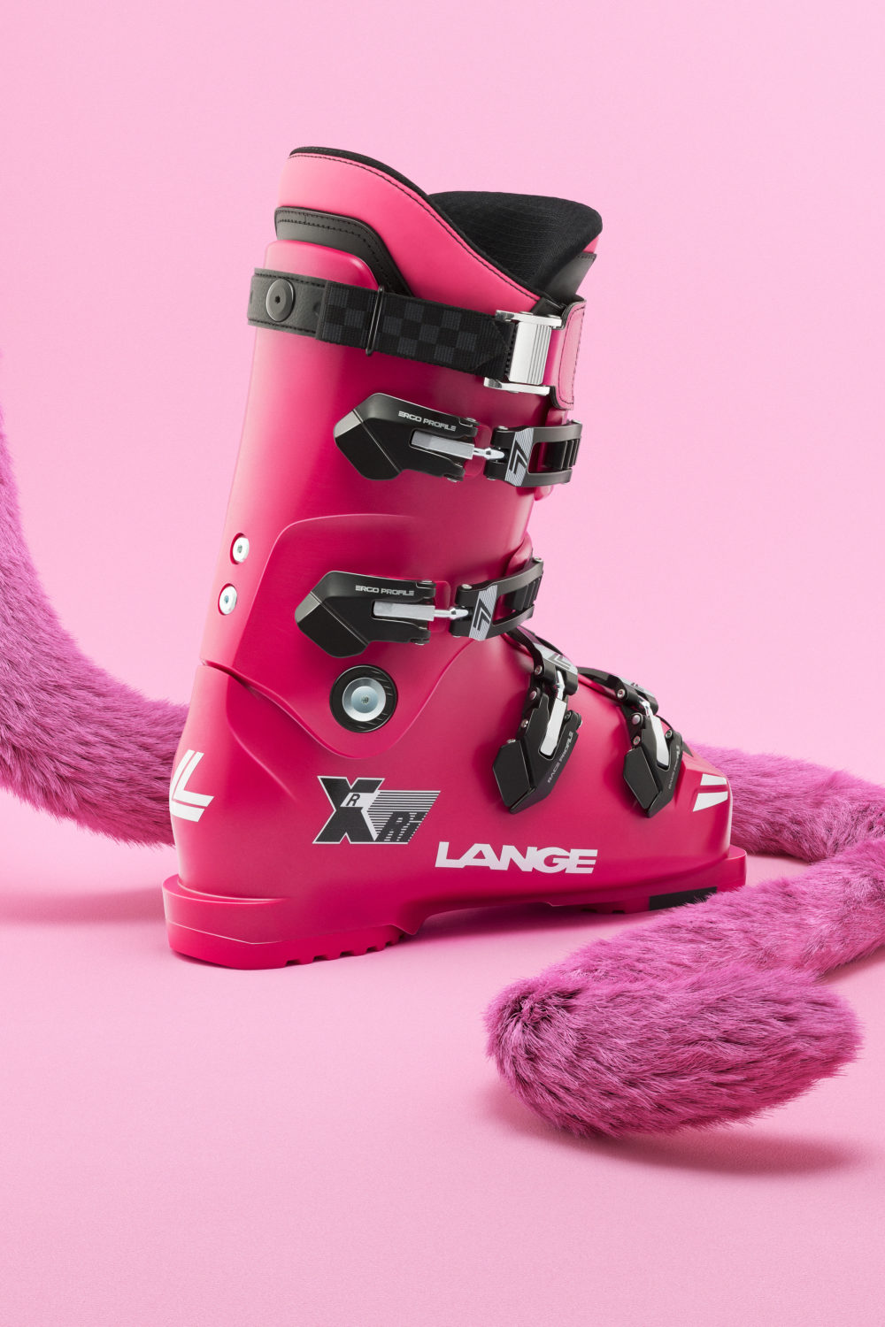 Lange Heritage Rx Ri Ein pinker Skischuh der Marke Lange steht vor einem pinken Hintergrund, umgeben von einer pinken, fellartigen Dekoration.
