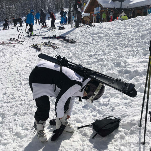 Skifahrerin mit Ausrüstung Skifahrerin beugt sich vor, um Skischuhe zu befestigen, Ski mit Skiback auf dem Rücken. Verschneite Landschaft.