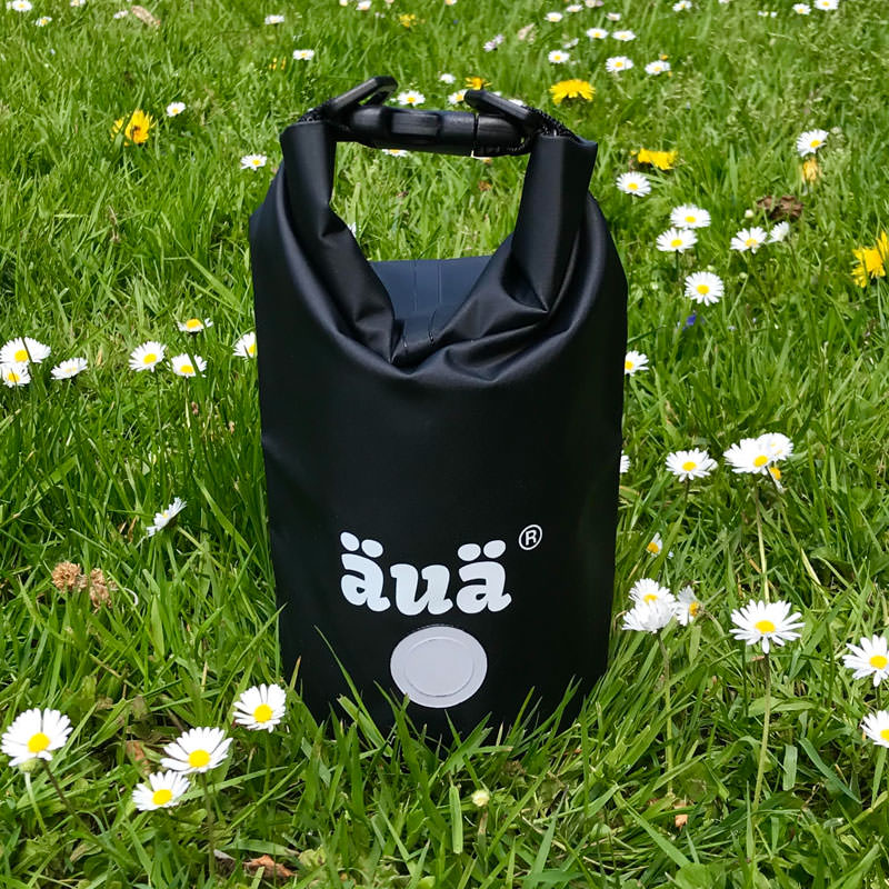 Schwarzer Dry Bag mit Logo im Gras, verschlossen mit Tragegriff.