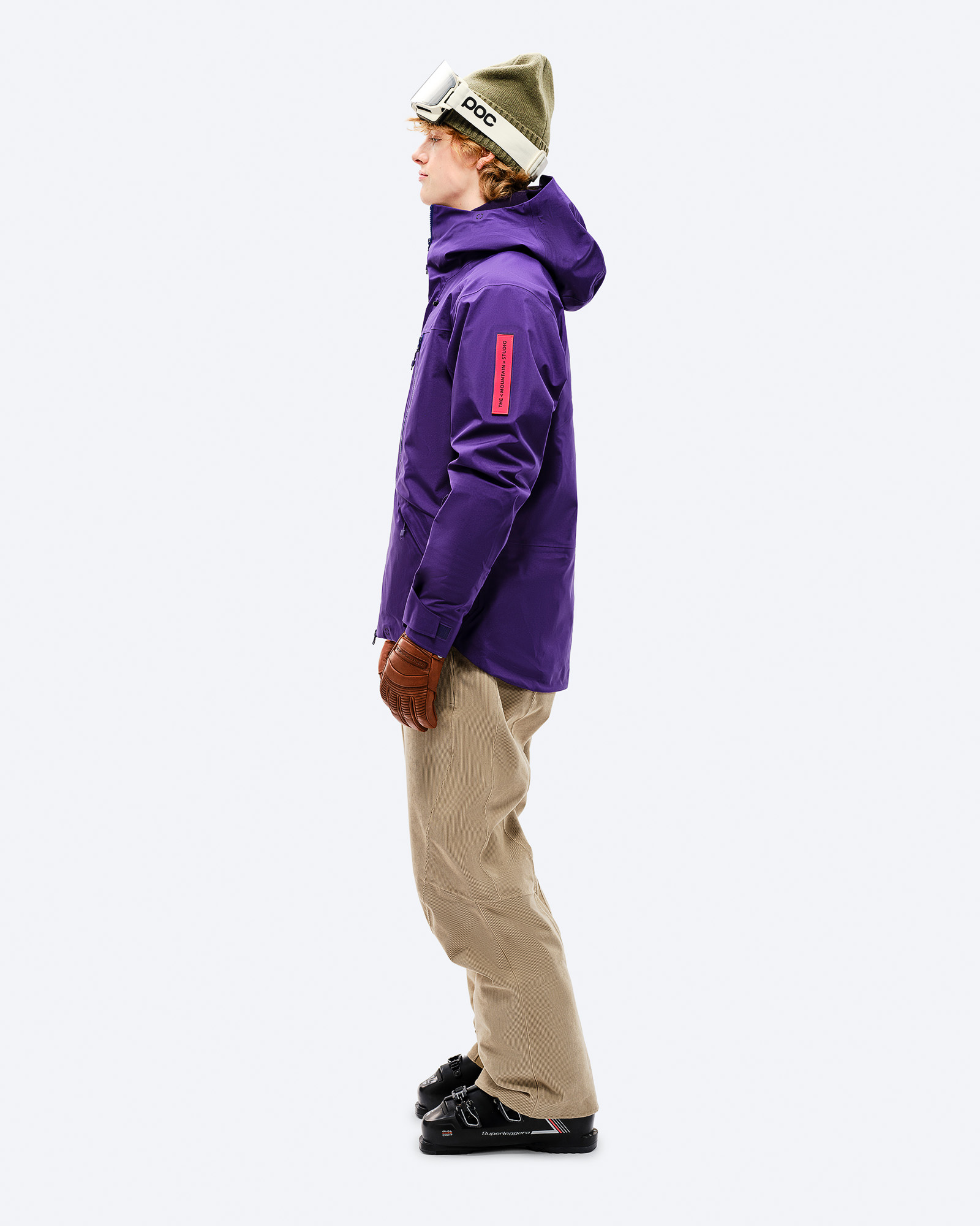 Lila GORE-TEX Skiausrüstung Person in lila GORE-TEX EPE 3L Shell Jacket, Skihose, Handschuhe und Skischuhe, seitliche Ansicht.