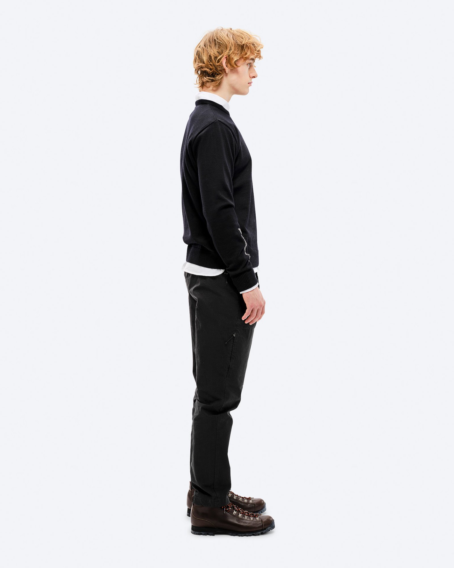 Männlicher Ski-Look Ein Mann im Profil trägt einen schwarzen K-3 Ski Sweater aus Merinowolle, dazu dunkle Hosen und braune Wanderschuhe.