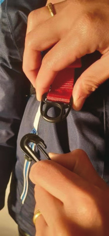 Leine am Ski Trainer Detailaufnahme: Hände befestigen rote Leine mit Karabiner am Ski Trainer Geschirr. Fokus auf Verschlussmechanismus.