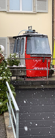 Rote Gondel im Schnee Eine rote Gondel "Männlichen" steht vor einem Haus bei leichtem Schneefall.