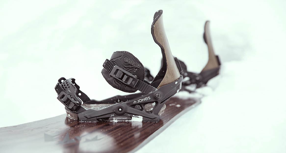 Nahaufnahme einer Snowboard-Bindung von Jones auf einem Snowboard im Schnee. Die Bindung ist schwarz mit braunen Akzenten.