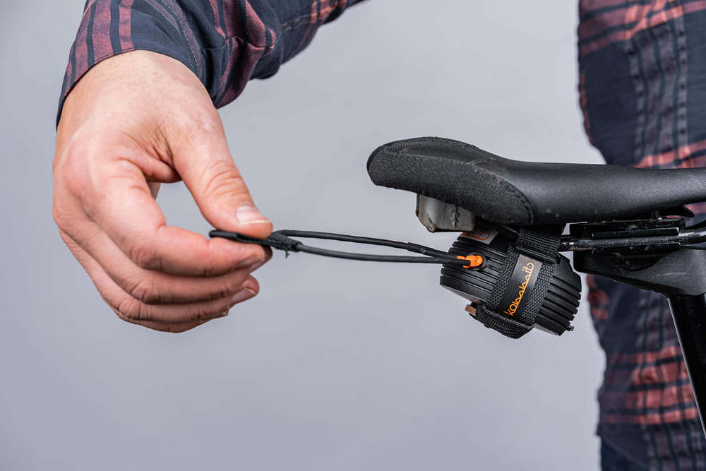 Nahaufnahme vom kommit Zugsystem am Fahrradsattel. Eine Hand hält das Zugseil bereit für die Anwendung.