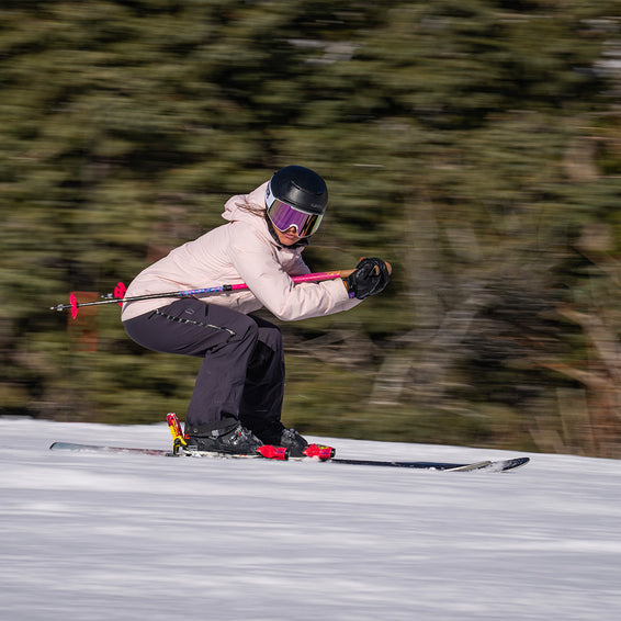 Skifahrerin mit pinker Miami Nights Proform Goggle auf der Piste, verschwommener Hintergrund.