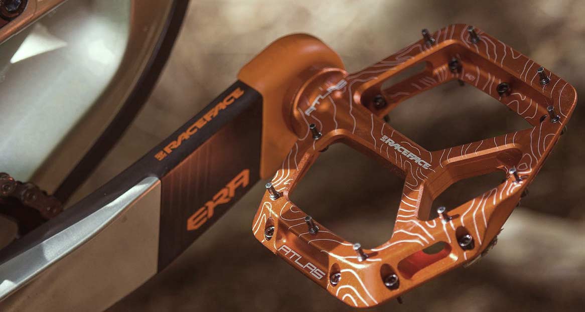 Nahaufnahme eines orangefarbenen Fahrradpedals mit weißen Höhenlinien und Stiften, montiert an einer ERA Kurbelgarnitur.