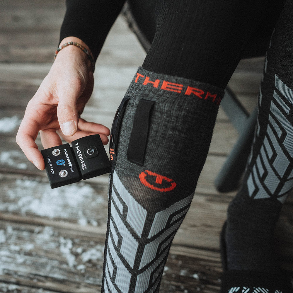 Thermic Ultra Warme Socke Person zeigt Thermic Ultra Warm Socke mit S-Pack 1400 Batterie in der Hand.