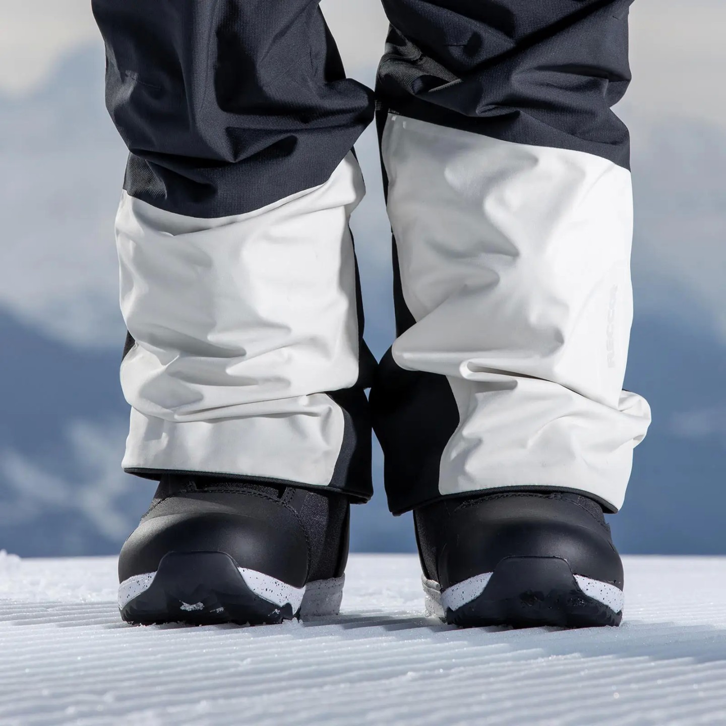 Beine mit Snowboardschuhen auf Schnee. Hosenbeine teils in Weiss über die schwarzen Nidecker Rift W Schuhe gezogen.