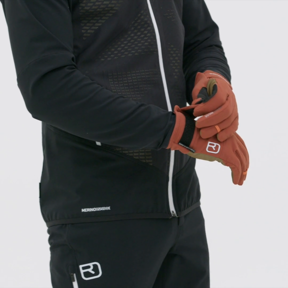 La personne enfile des Glove Liner Rock'n'Wool de couleur rouge-brun et porte des vêtements de sport noirs.