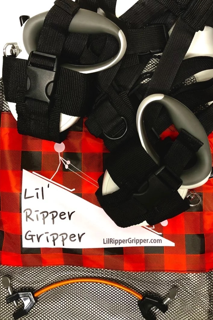 Lil' Ripper Gripper Detail Lil' Ripper Gripper: Detailaufnahme der Ski-Lernhilfe mit Leinen, Gurt, Griffen und Skispitzenhalter auf rot-schwarz kariertem Stoff.