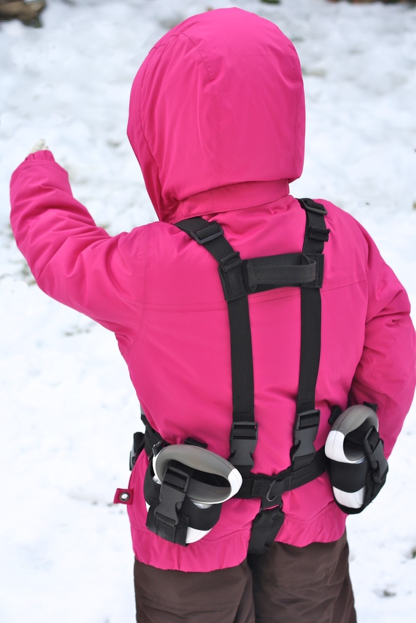 Kind im Schnee Kind mit rosa Jacke und Lil' Ripper Gripper Skilernhilfe am Rücken im Schnee.