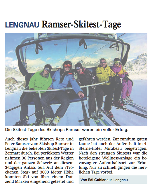 Gruppe von fünf Personen mit Skiern in einem Sessellift vor schneebedeckten Bergen.