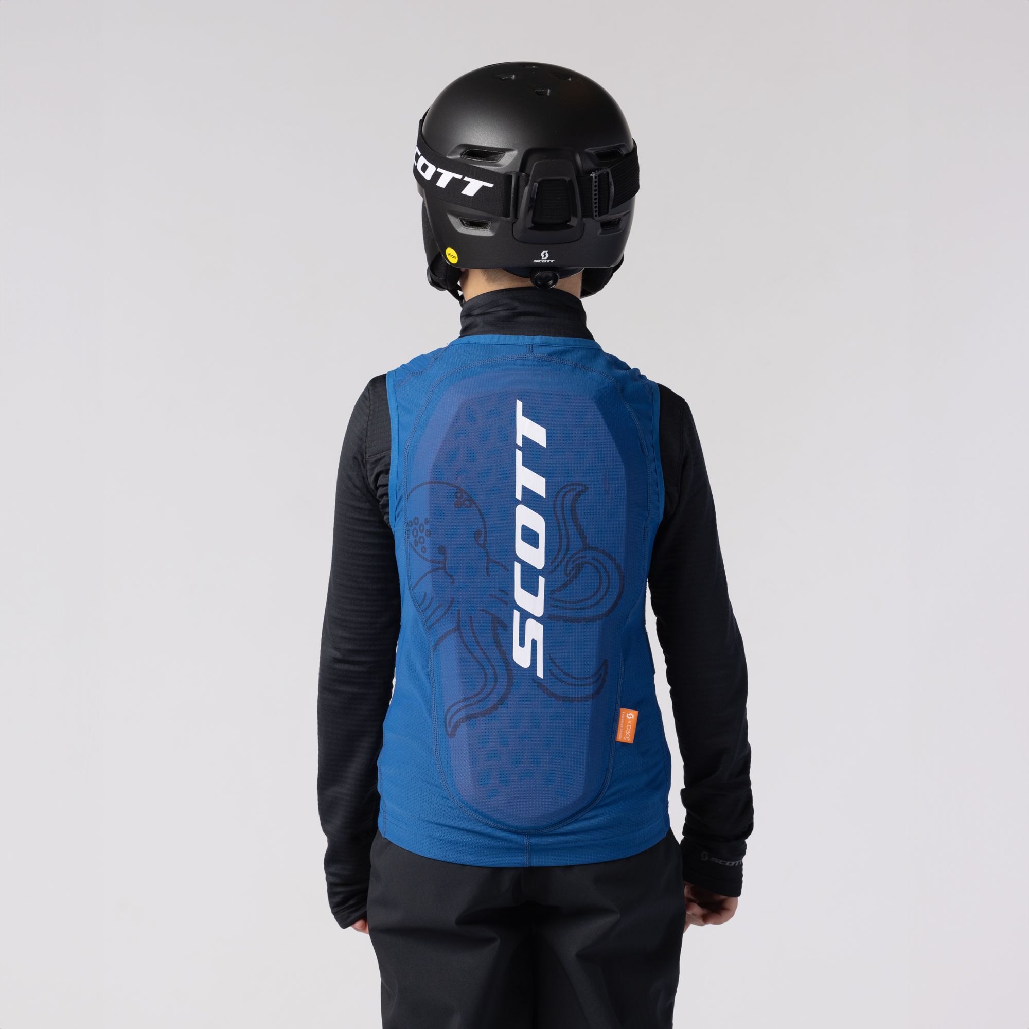 Kind mit Oktopus-Weste Rückenansicht eines Kindes mit Helm und blauer SCOTT Airflow Junior-Weste mit Oktopus Grafik.