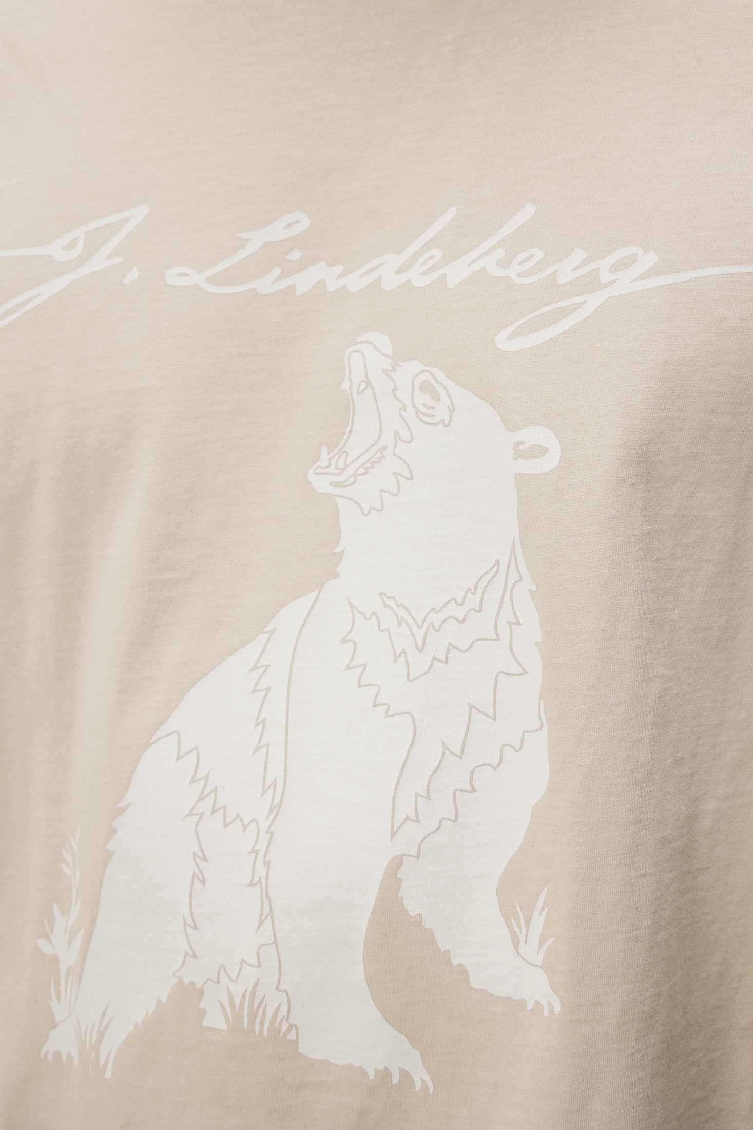 Detailaufnahme eines T-Shirts in Oyster Gray, bedruckt mit einem Bären und dem Schriftzug "J. Lindeberg".