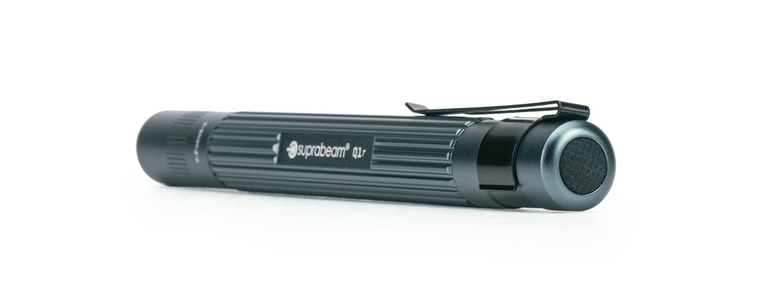 Suprabeam Q1r Stiftlampe Eine Suprabeam Q1r Stiftlampe liegt waagerecht auf einem weißen Hintergrund. Sie ist dunkelgrau mit einem Clip.