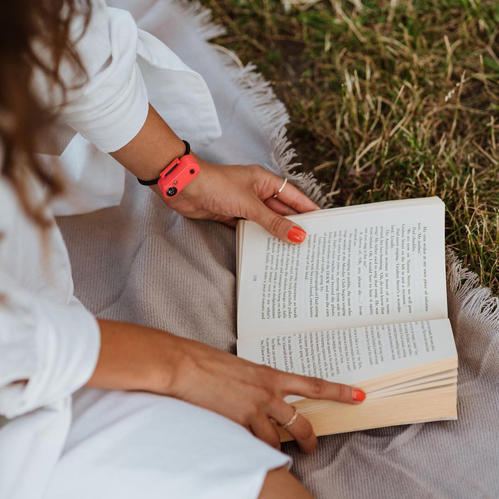 Person liest im Freien ein Buch mit "Tickless Active" am Handgelenk. Fokus auf den Schutz beim aktiven Lesen.