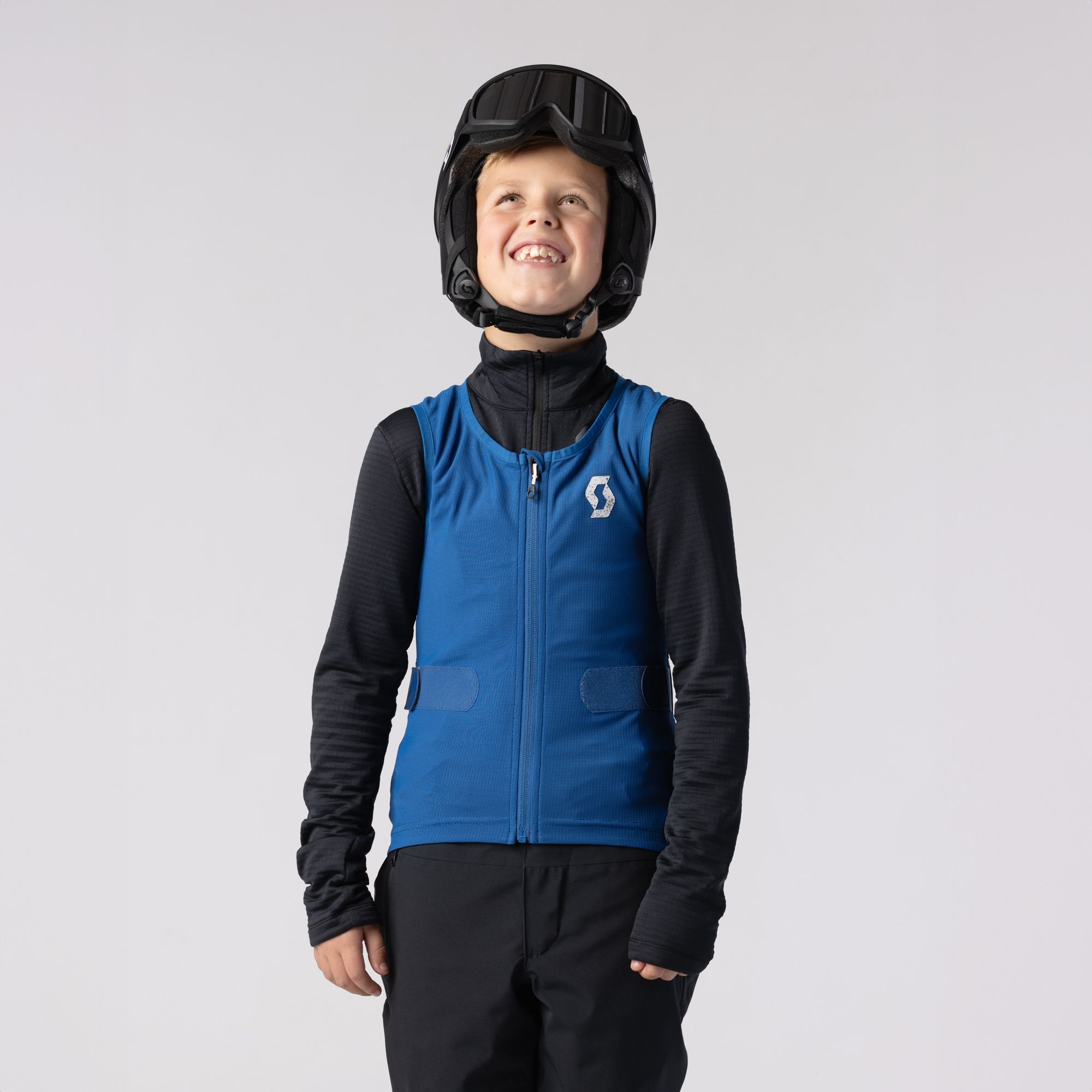 Lächelnder Junge in SCOTT-Weste Ein lächelnder Junge mit Helm und Skibrille trägt eine blaue SCOTT Airflow Junior-Weste.