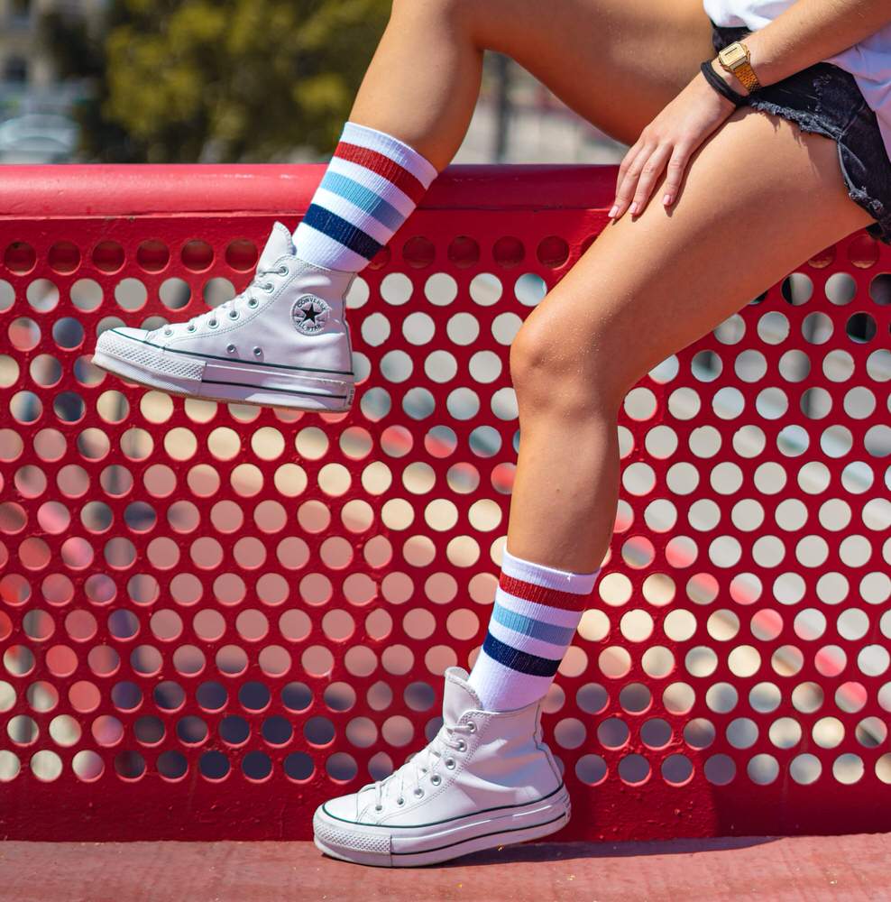McFly II Socken Stil Person mit McFly II Mid High Socken und weißen Schuhen vor rotem Hintergrund.