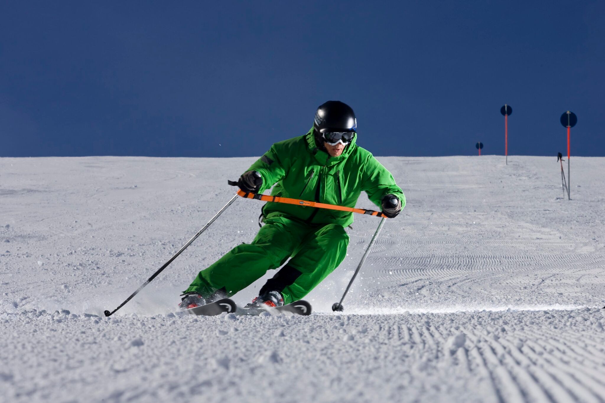 Skifahrer in grüner Kleidung mit Training Strap auf präparierter Piste.
