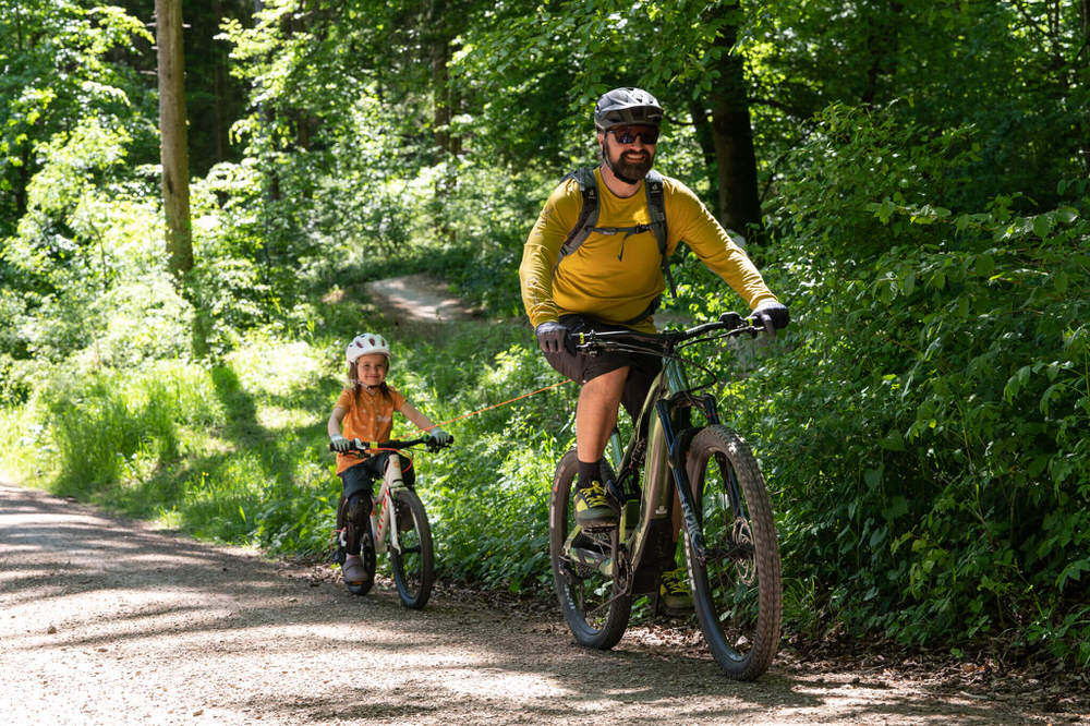 Vater zieht Kind mit dem kommit Zugsystem beim Fahrradfahren auf einem Waldweg.