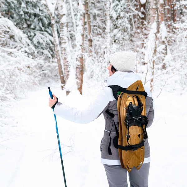 Schneeschuh-Rucksack Frau mit Schneeschuhen auf dem Rücken und Skistock im Schnee. Raq Back Rucksack für Schneeschuhe.